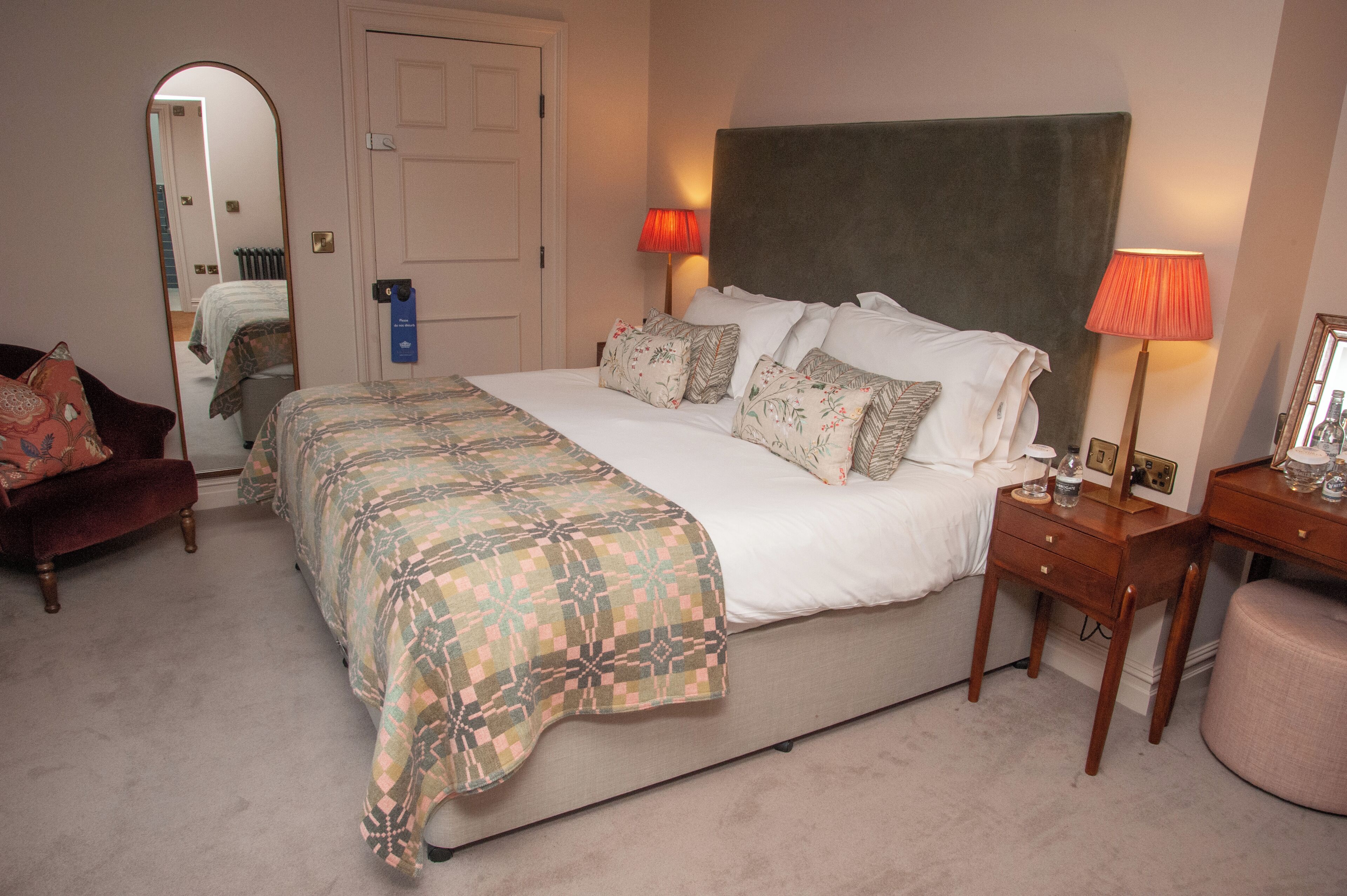 Une chambre à coucher bien rangée, avec un grand lit, des lampes de chevet, un miroir et une petite table avec une lampe.