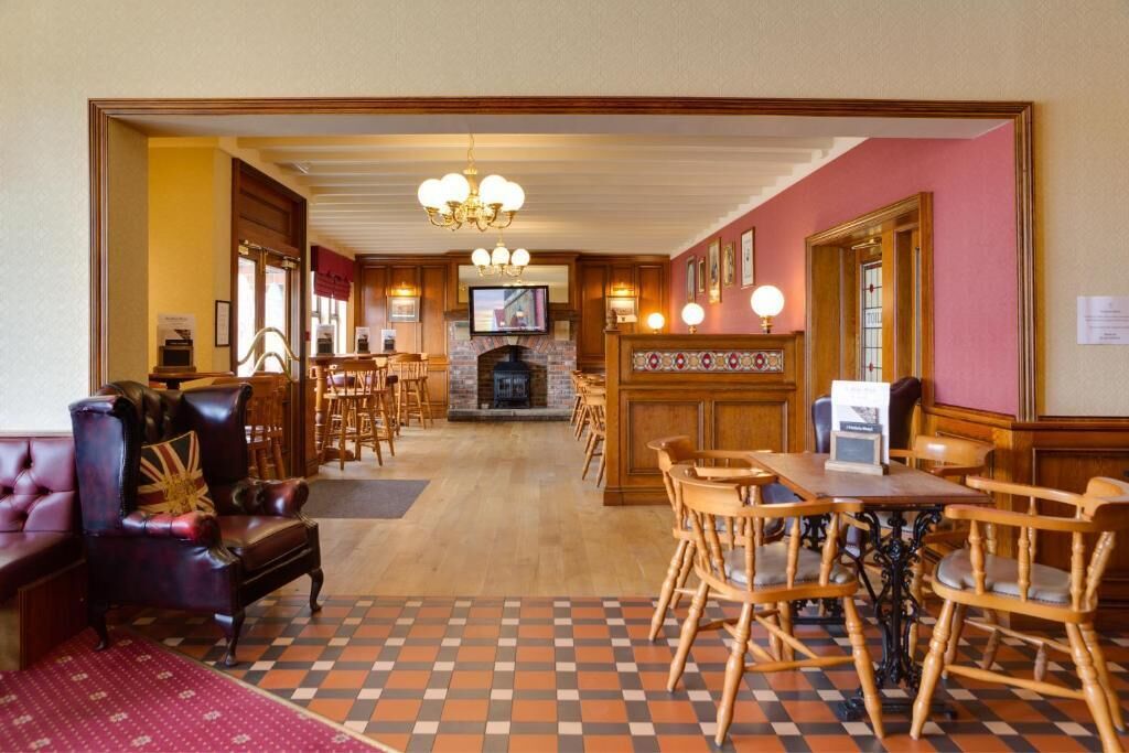 A hotel lobby with a checkered floor, leather armchairs, wooden tables, a fireplace, and a television.