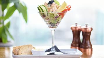 Salada numa taça de vidro com pão e um pequeno prato de molho sobre uma mesa de madeira.