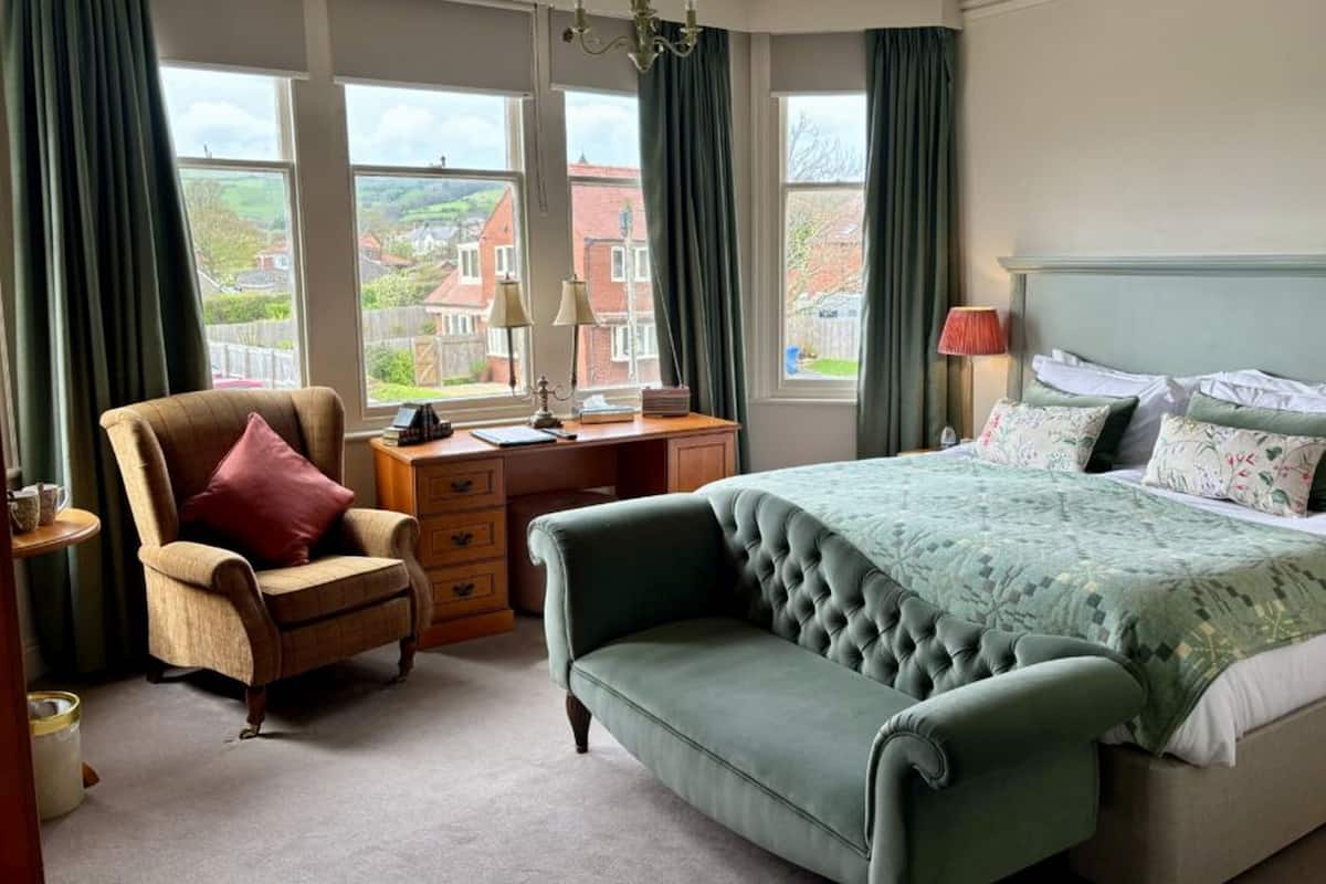 A bedroom with a bed, a chair, a desk, and a view of the outside.