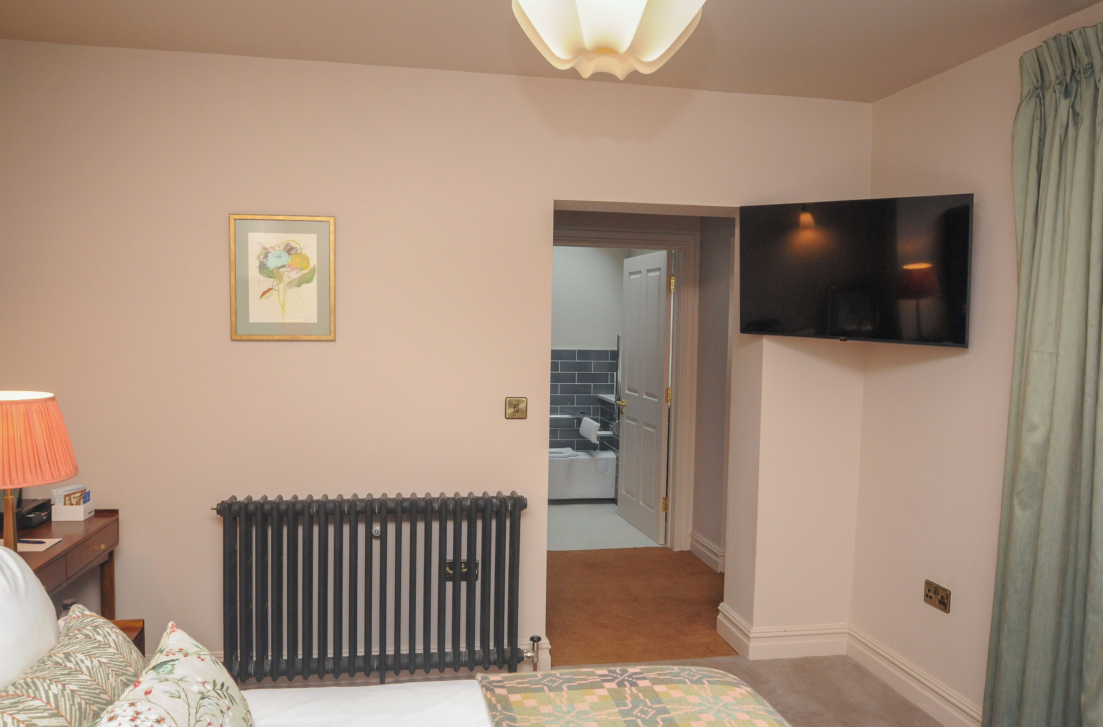 A hotel room with a bed, a radiator, a television, and a bathroom visible through an open door.