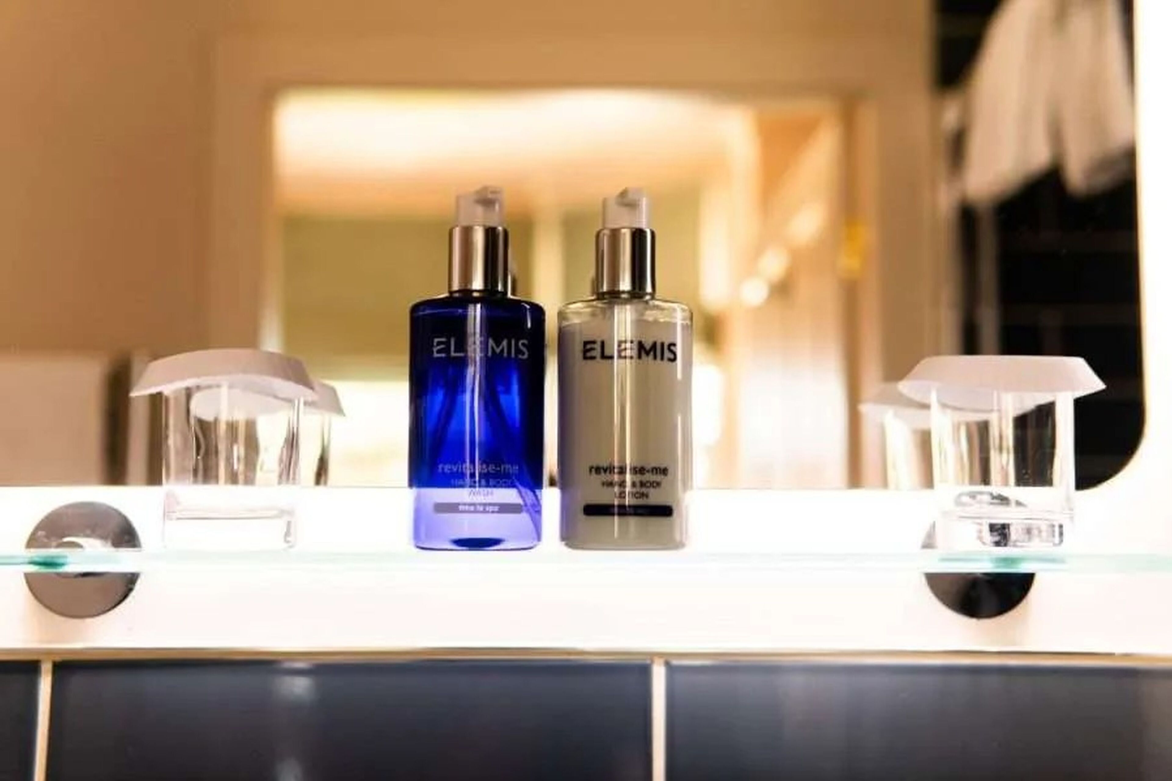 Dos botellas de crema corporal Elemis Revitalize Me sobre una encimera de baño.