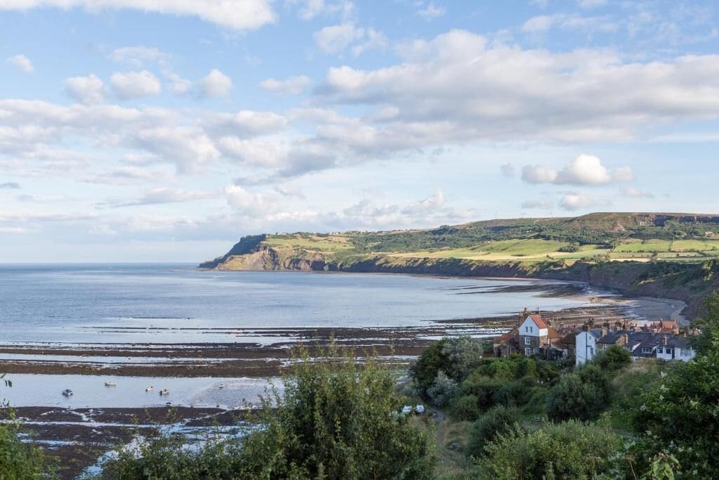 A coastal landscape with a view of the sea, cliffs, and a small settlement with houses.