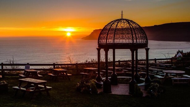A gazebo with a metal lattice roof overlooking a body of water at sunset. - Hotel Victoria (Whitby)