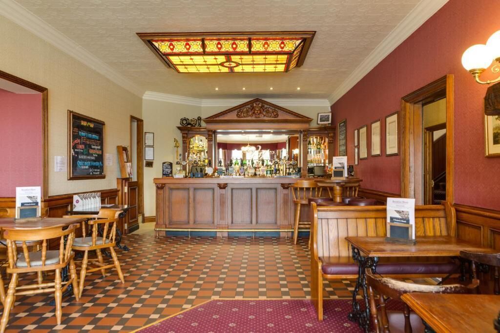 A bar area with wooden furniture, a checkered floor, and a stained glass ceiling.