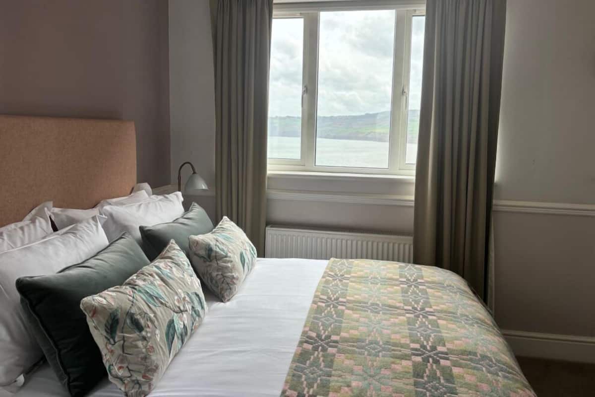 A hotel room with a bed, a window with curtains, and a view of the sea.