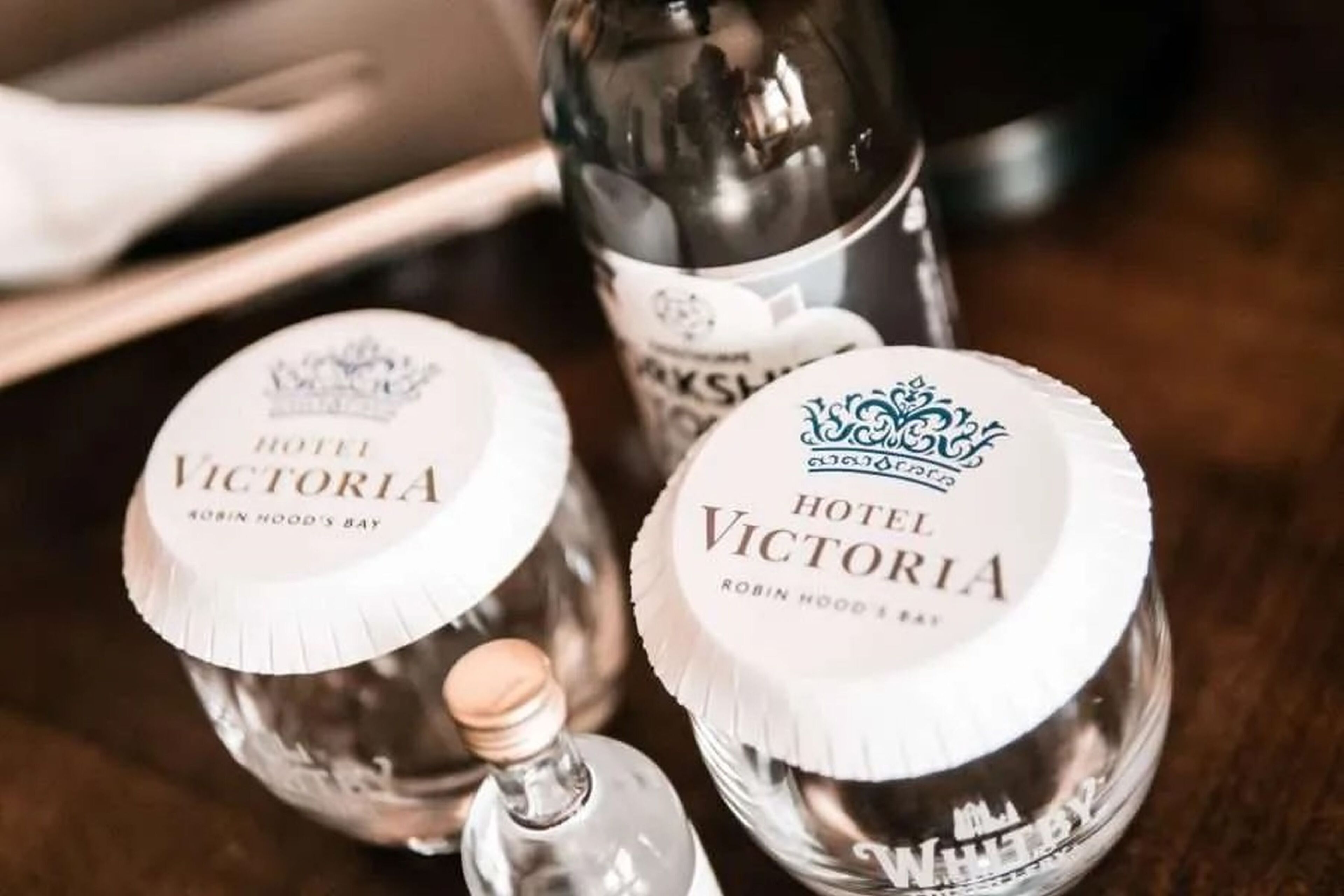 Kolme Hotel Victoria -ginipulloa etiketteineen, aseteltuna puupinnalle.