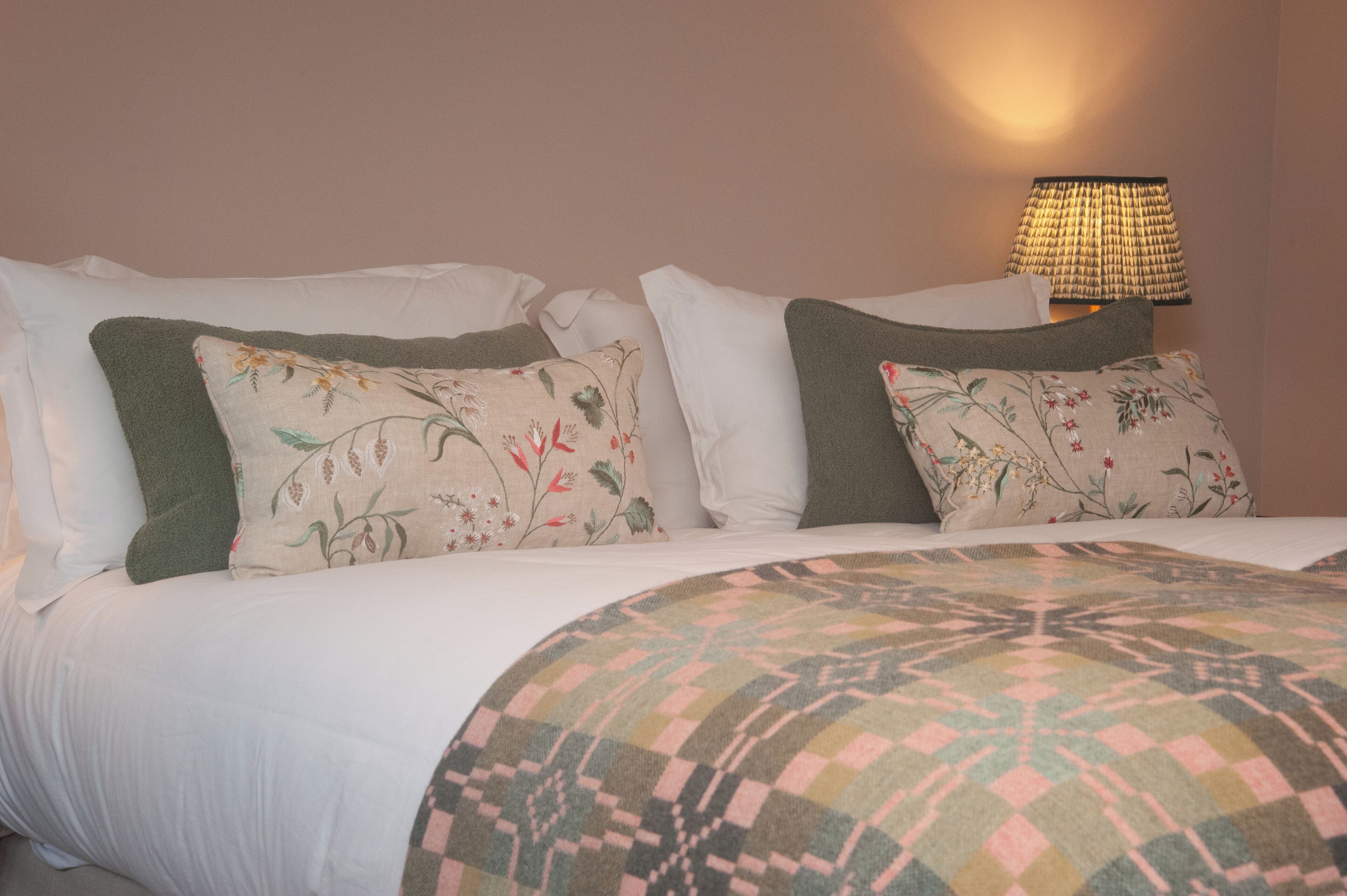 Cama bem arrumada com almofadas de estampas florais e geométricas, edredom branco e manta estampada.