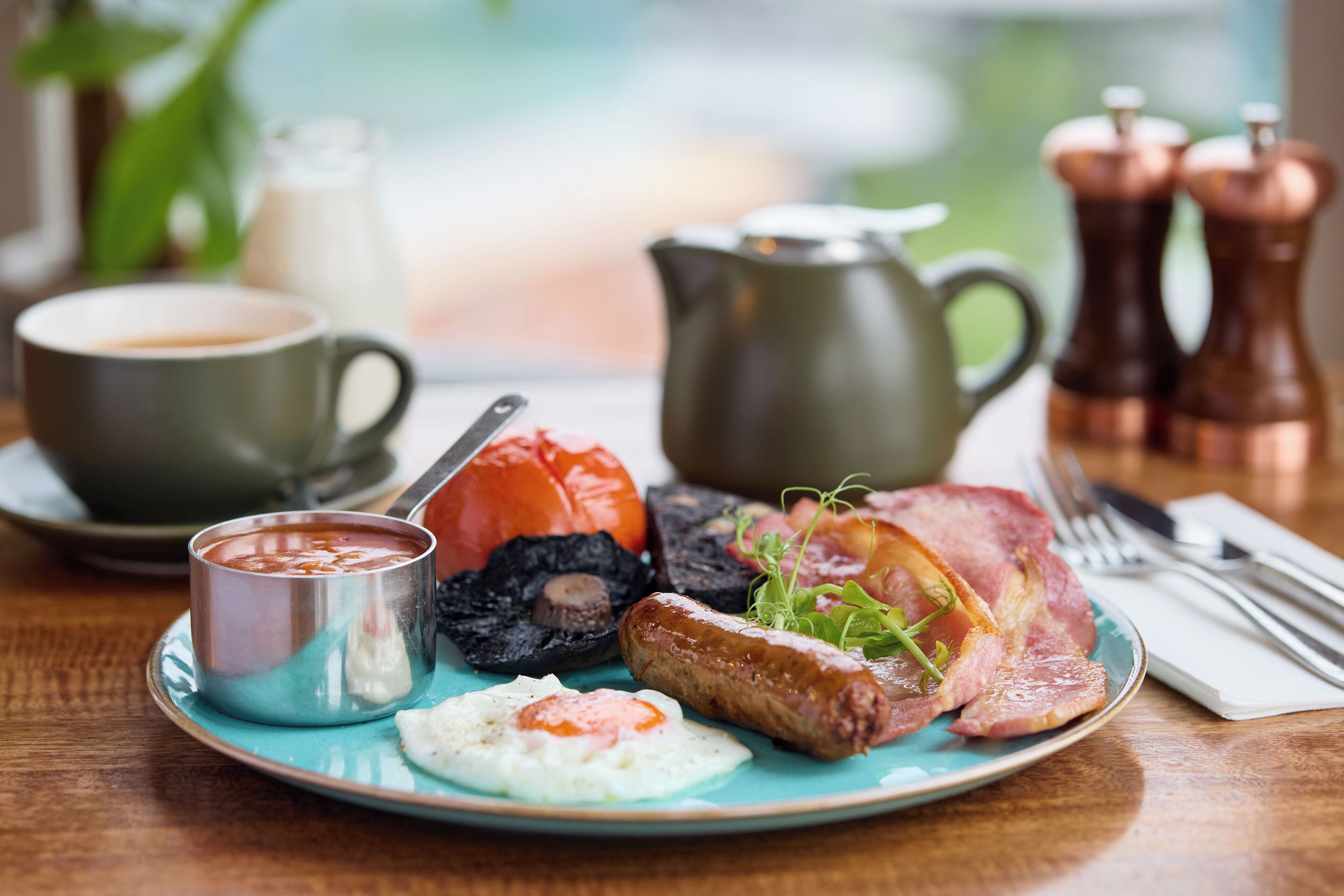 Un piatto per la colazione con uova, salsicce, pancetta e un peperone rosso.