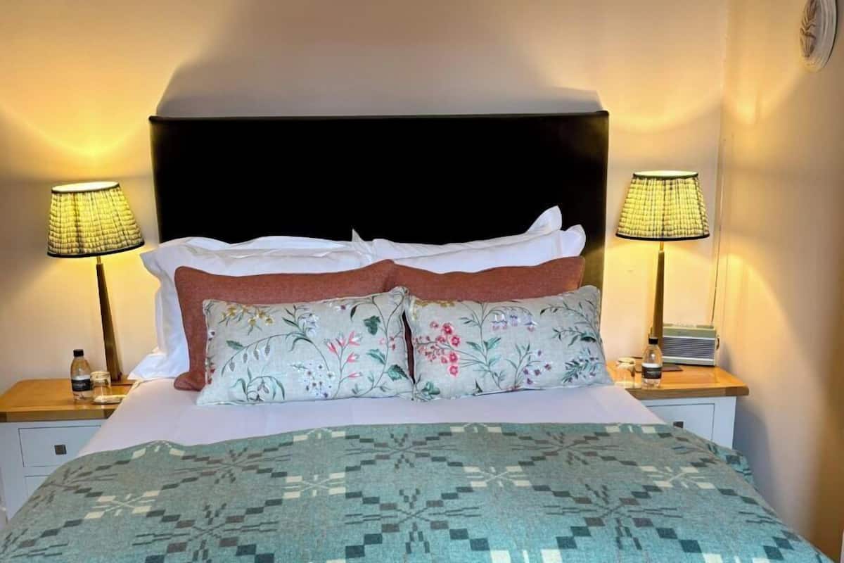 A neatly made bed with a patterned bedspread, two bedside lamps, and a nightstand with a bottle and a glass.