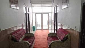 A hallway with two rows of upholstered chairs with red cushions, a red carpet, and a ceiling fan.