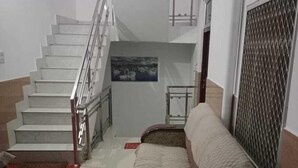 A staircase leading to an upper floor, a red carpet, and a sofa in a room with white walls and a metal grille.