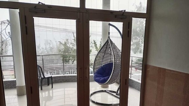 A room with a sliding glass door leading to an outdoor balcony with a hanging chair and a green chair.