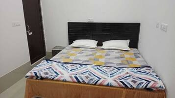 Una cama individual con una colcha estampada y dos almohadas, un cabecero de madera, una mesita de noche y una puerta con cerradura.