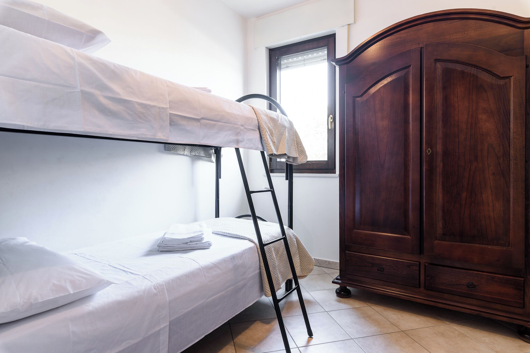 Ein Stockbett mit weißer Bettwäsche, ein Holzschrank und ein Fenster mit Jalousien.