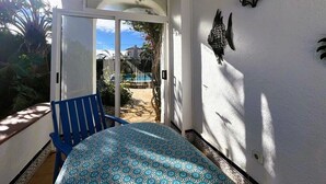 Ein Zimmer mit einem Bett, einem blauen Sessel, einer Wandleuchte und Blick auf ein Schwimmbad und Grünflächen.