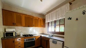Eine Küche mit Holzschränken, einer Mikrowelle, einem Herd, einem Backofen, einer Spüle und einem Kühlschrank.