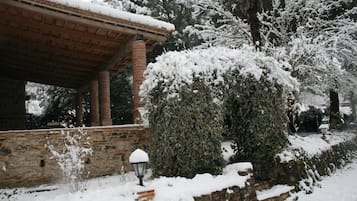 A stone building with a brick roof covered in snow, surrounded by snow-covered trees and bushes.