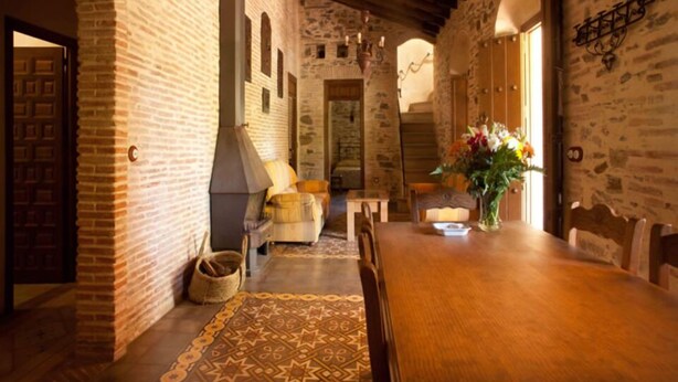 Un intérieur rustique avec un mur en pierre, un plafond en bois et un coin repas comprenant une table et des chaises.