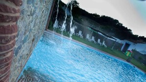 Une piscine dotée de jets d’eau, entourée d’un mur de briques et d’une pelouse aménagée avec des chaises longues.
