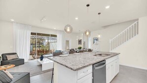 Una cocina moderna con una isla central, armarios blancos e iluminación colgante.