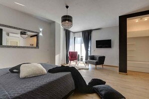 A modern bedroom with a large bed, a red armchair, a black armchair, a chandelier, and a flat-screen TV. - Villa with heated pool, jacuzzi and sauna (Rovinj)