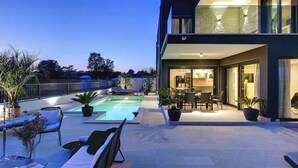 Una casa moderna con piscina, mobiliario de exterior y una zona de patio bien iluminada.