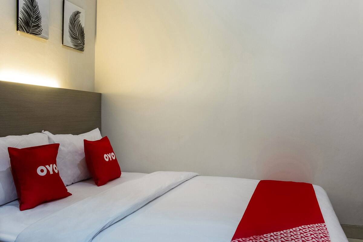 A neatly made bed with white and red bedding, two pillows with the word "OYO" on them, and a red blanket.