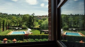 A view of a swimming pool with lounge chairs and umbrellas, surrounded by well-maintained hedges and trees, with a distant view of a town. - Rustico Relax Explore Tuscany (Santa Maria)