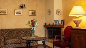 A cozy living room with a floral-patterned sofa, a small table with a vase of flowers, a red armchair, a fireplace, and a lamp. - Rustico Relax Explore Tuscany (Santa Maria)