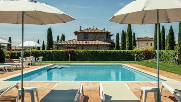 A swimming pool with lounge chairs and umbrellas, surrounded by a hedge and a stone building in the background. - Rustico Relax Explore Tuscany (Santa Maria)