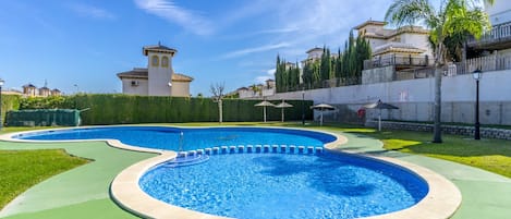 A swimming pool with a curved design, surrounded by a green deck and a low wall.