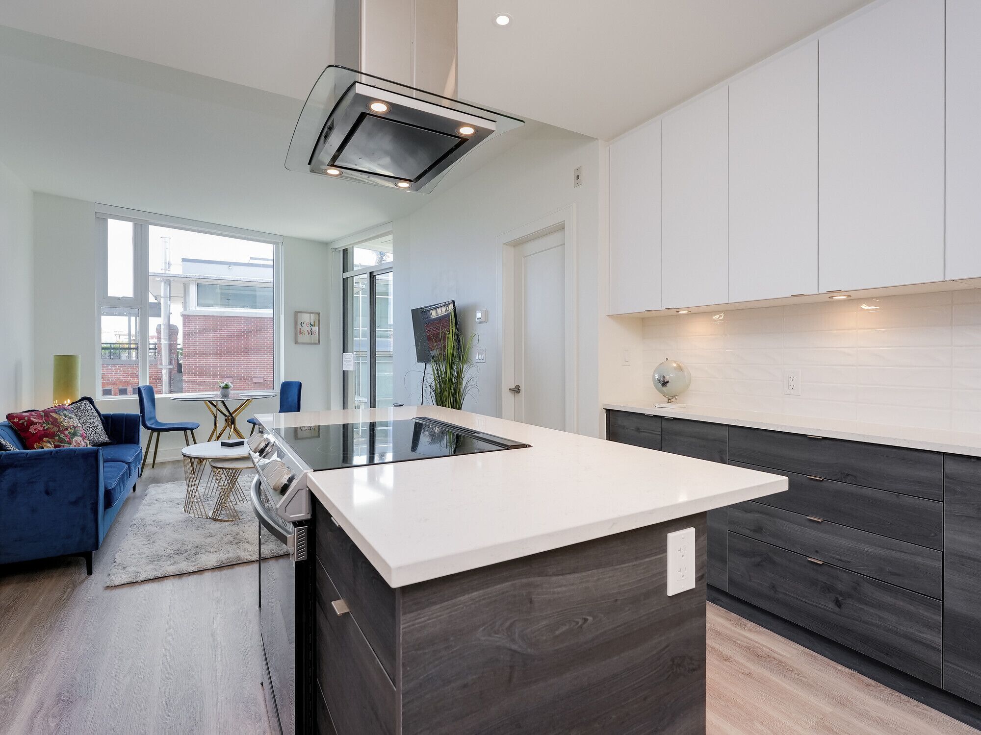 Cocina moderna con una isla central, muebles de madera oscura y encimera blanca.