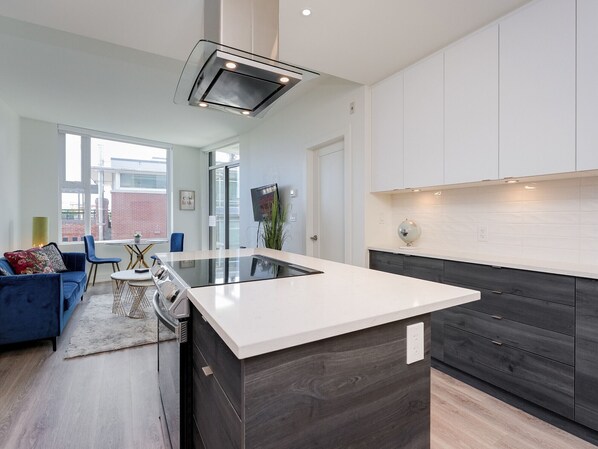 Cocina moderna con una isla central, muebles de madera oscura y encimera blanca.