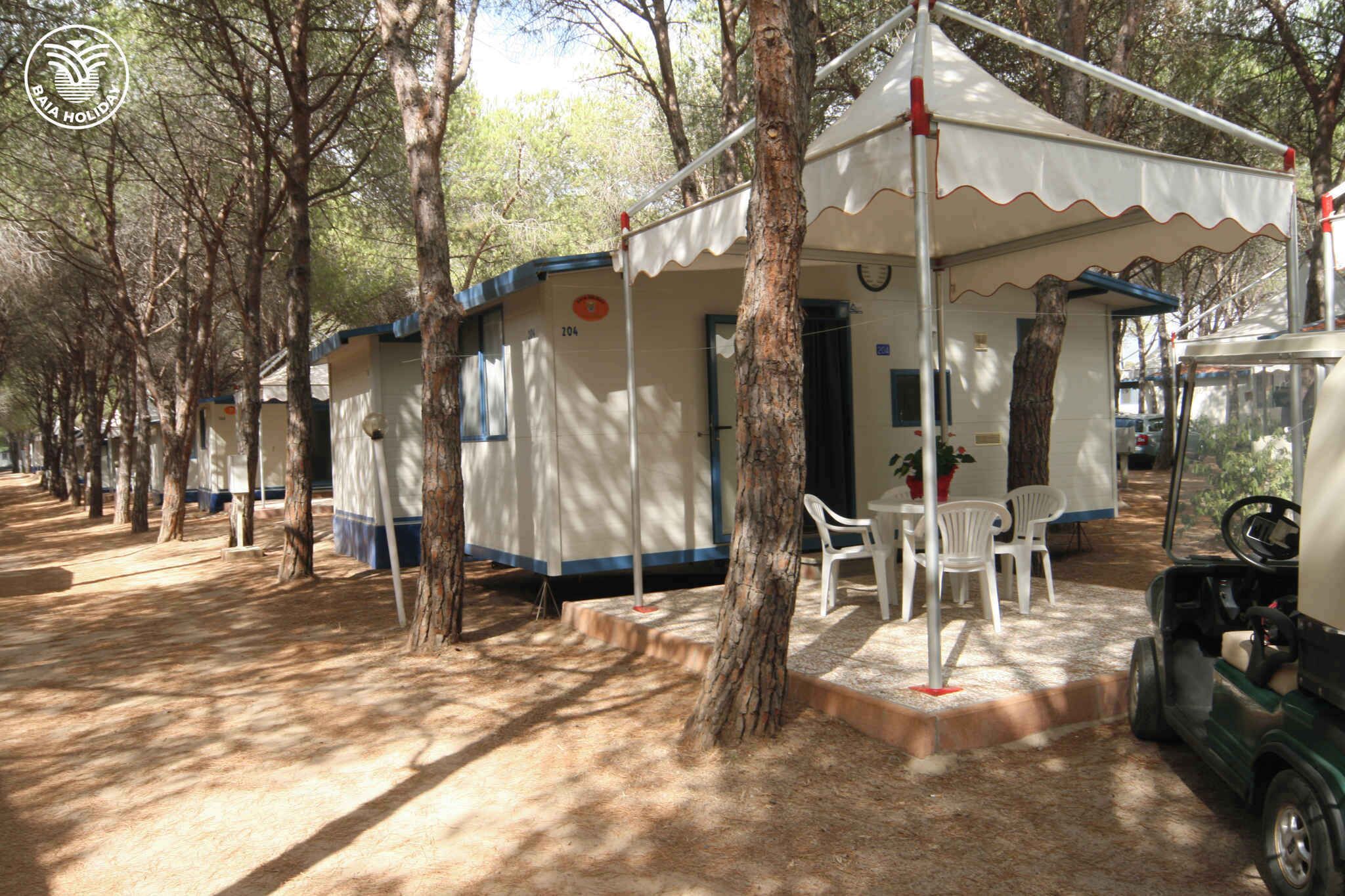 Una hilera de cabañas arboladas con una estructura tipo carpa, una mesa, sillas y un carrito de golf.