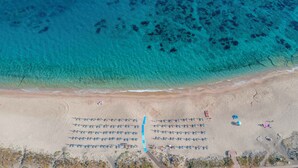Vista aerea di una spiaggia con file di lettini e alcune persone sparse.