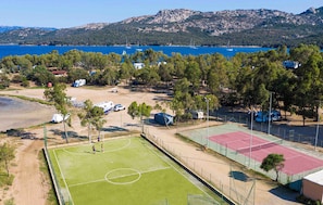 Ein Sportkomplex mit mehreren Tennisplätzen, einem Fußballfeld und einem Parkplatz, auf dem Wohnmobile stehen.