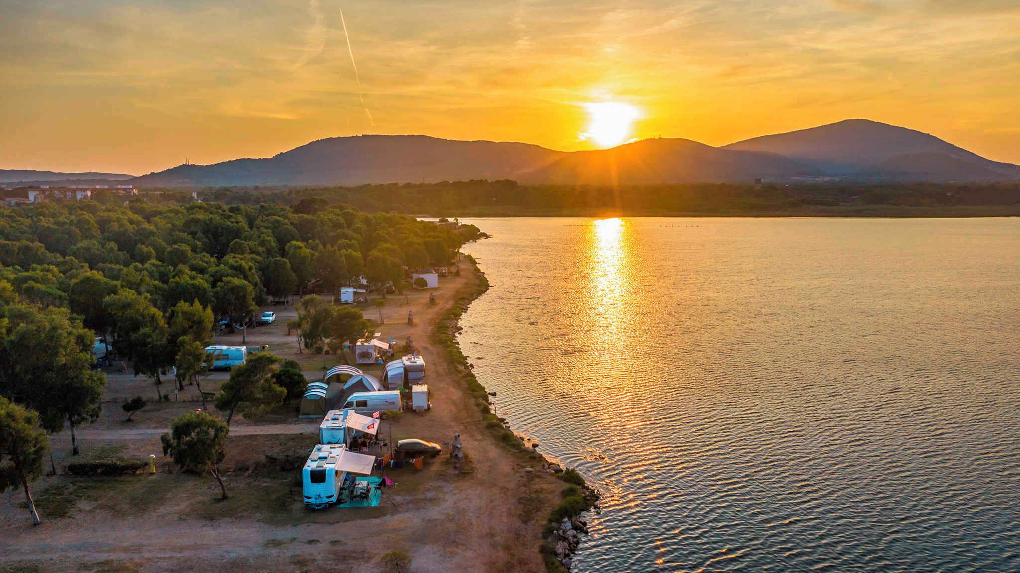 An aerial view of a lakeside campsite with RVs and tents, surrounded by trees and hills.