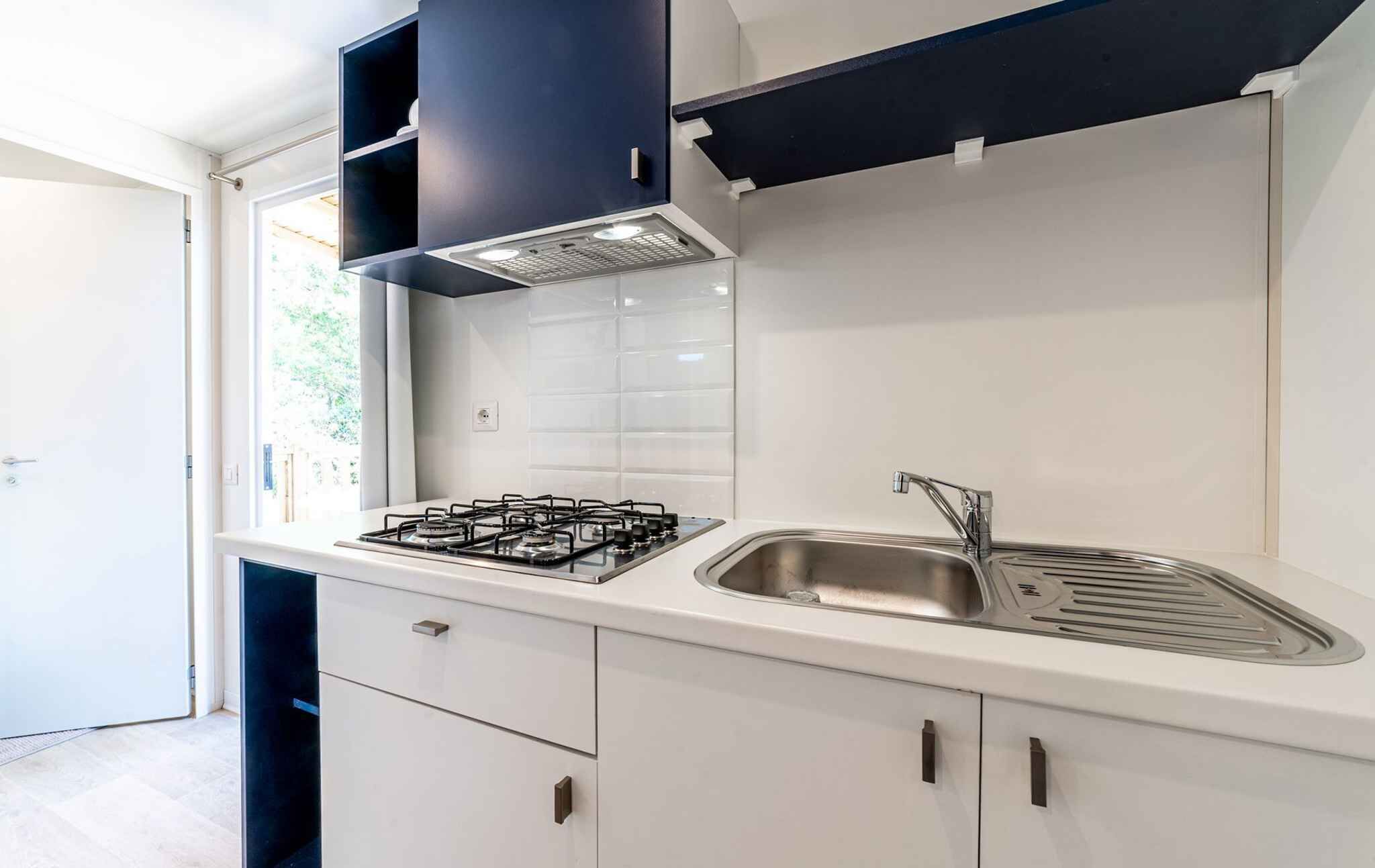 A modern kitchen with a gas stove, stainless steel sink, white cabinets, and a black hood.
