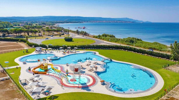 Una gran piscina al aire libre con varias toboganes y un área circundante con sillones y sombrillas.