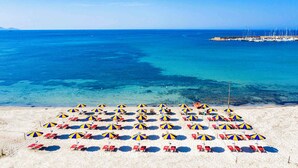 Una playa con filas de tumbonas y sombrillas, un mar azul cristalino y un muelle a lo lejos.