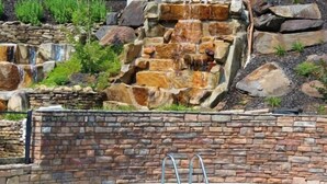 A swimming pool with a stone waterfall feature and a stone wall. - Mountain Eden, Hot Tub, Resort Pool, WIFI, $560 FREE tickets each paid day!!! (Gatlinburg)