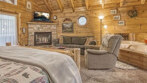 A cozy log cabin interior with a fireplace, a sofa, a chair, and a large bed. - Mountain Eden, Hot Tub, Resort Pool, WIFI, $560 FREE tickets each paid day!!! (Gatlinburg)