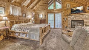 A log cabin bedroom with a bed, a fireplace, a television, and a large window. - Mountain Eden, Hot Tub, Resort Pool, WIFI, $560 FREE tickets each paid day!!! (Gatlinburg)