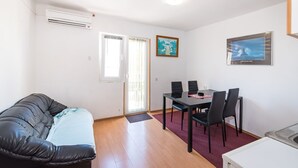 A room with a sofa, a dining table with chairs, a small kitchen area, and a door with a window.
