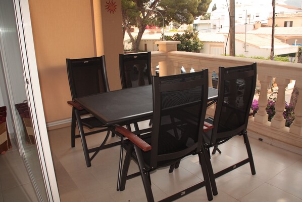 Un balcon avec une table et des chaises, une vue sur la rue et un immeuble en arrière-plan.