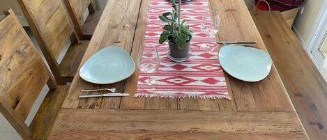 A wooden dining table with two plates, a glass, a potted plant, and a patterned placemat.