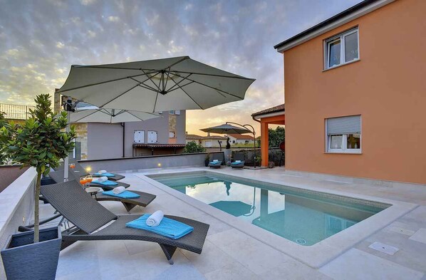 A rooftop pool with lounge chairs and umbrellas, surrounded by buildings.