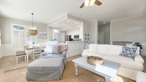 Un salon spacieux avec un canapé blanc, un pouf gris et une table basse blanche.