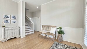 Un couloir avec un banc en bois, une console blanche, un escalier et des tableaux encadrés accrochés au mur.